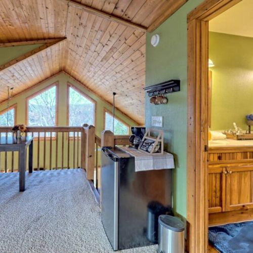 mini fridge in loft area with a desk seated overlooking the living area with a wall of windows