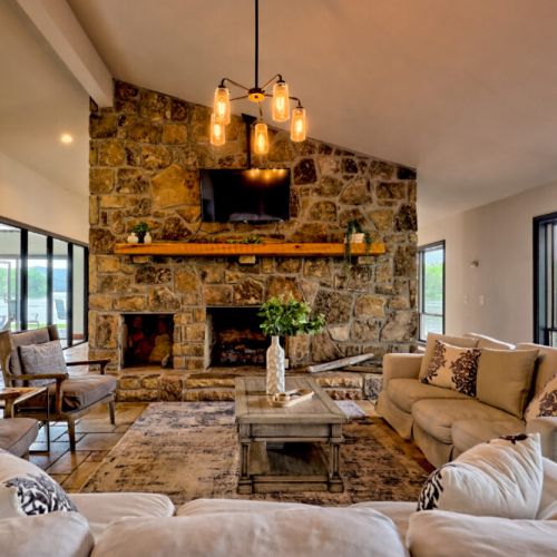 Living room area with large stone fireplace, floor to ceiling windows to watch those in the pool or out the front area of the home.